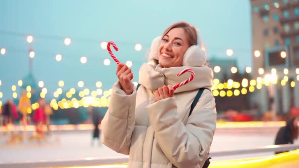 Woman in Earmuffs Standing Outdoor Near Ice Skating Rink on Central City Square at Winter Holiday