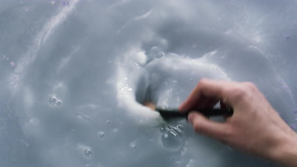 Stirring Dissolved Bath Bomb in Water with Brush Closeup