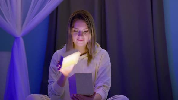 Happy Young Woman Opening Beautiful Golden Christmas Gift Box with Magic Light