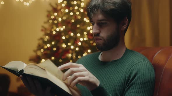 Boy reads book beside Christmas tree