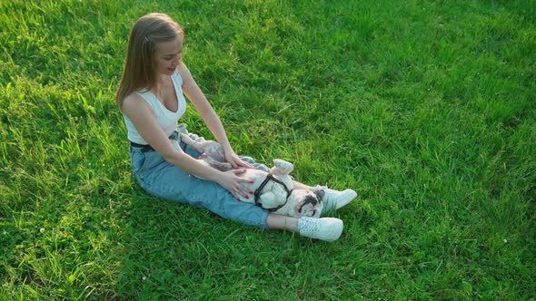 Young Woman Petting French Bulldog on Grass.