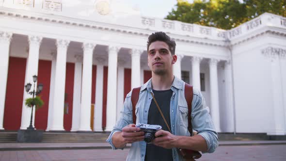 Young Attractive Handsome Man Tourist with Backpack Taking Photos on Vintage Camera in Old City