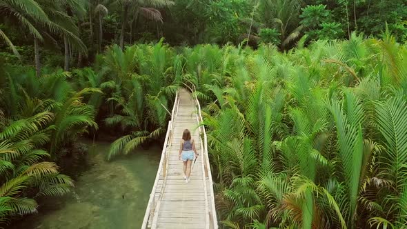 Aerial view of woman walking on long wooden bridge in Bojo river, Philippines.