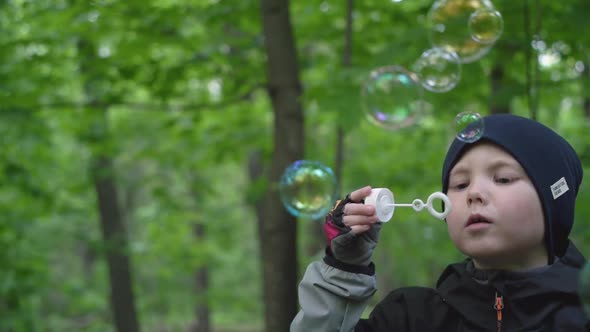 Portrait of a boy blowing soap bubbles in the forest