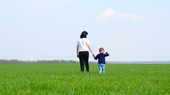 The Mother Leads Her Son By the Hand on a Green Field Against the Blue Sky