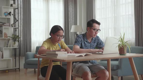 Asian Father Working With Laptop And Daughter Doing Homework At Living Room