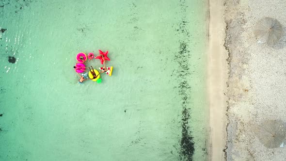 Aerial view of friends floating on inflatable mattresses in transparent sea.