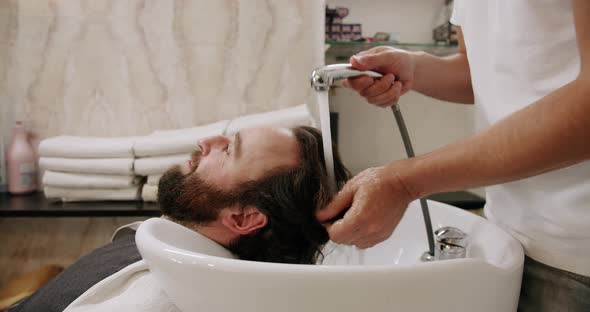 The Man in the Beauty Salon is Served Washing His Head with Shampoo and Water