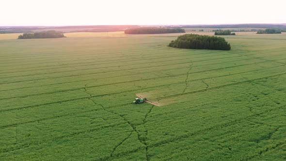 Aerial Tractor Trailer Sprays Mineral Fertilizer On Green Farm Field At Sunset