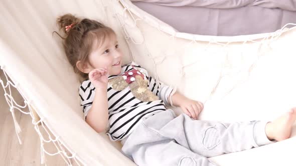 Little Smiling Girl Chilling and Swinging on a White Hammock