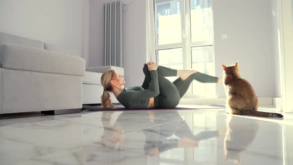 young fitness woman doing aerobics exercises lying on her back on floor a mat.