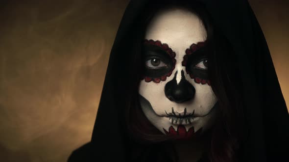 Woman in Black Hood and Santa Muerte Makeup Calmly Watches Straight