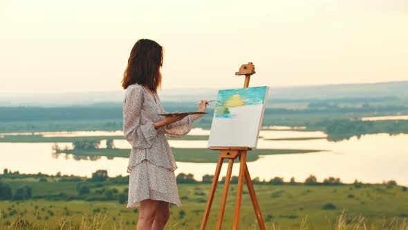 Young Woman Drawing a Painting on Sunset and Looks in the Camera