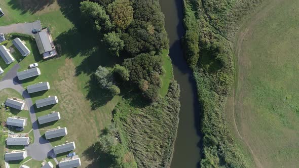 Top-down aerial of a river and the edge of a holiday caravan park. Ducks can just be made out swimmi