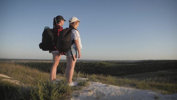 Mother and Daughter on Top of a Mountain. Hikers with Backpack Standing on Cliff and Looking To a