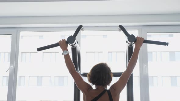 Mature Woman is Doing Pullups with Wide Grip in Gym Back View