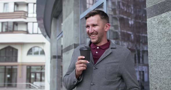 Happy Businessman Smiling at Camera and Drinks Cup of Coffee Near Office Centre