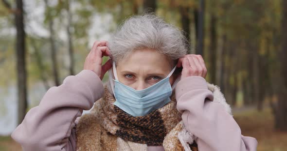 Portrait of an Adult Woman in a Forest Park, Elderly Woman Puts on Protective Medical Mask, Autumn