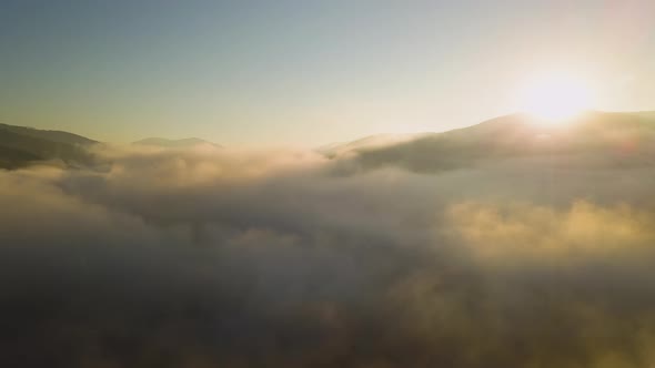 Aerial view of vibrant sunrise over white dense fog with distant dark silhouettes of mountain