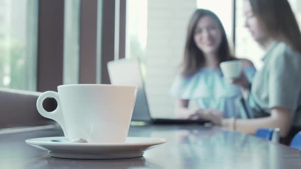 Cup of Coffee on the Table of Two Students Working on a Project on Background