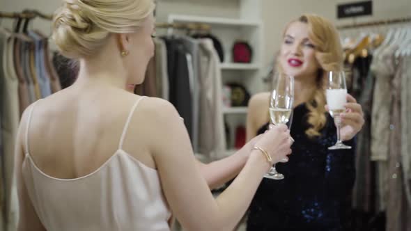 Three Positive Caucasian Women Clinking Glasses with Champagne in Fashion Boutique. Happy Rich