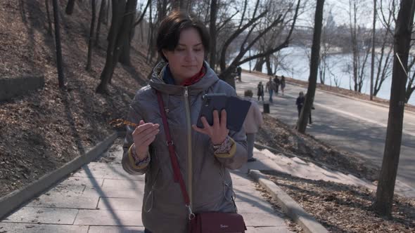 A Middleaged Brunette Caucasian Woman with Short Hair in a Brown Jacket Walks in the Park and Writes