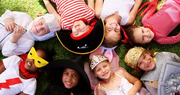 Group of kids in various costumes lying on grass alt