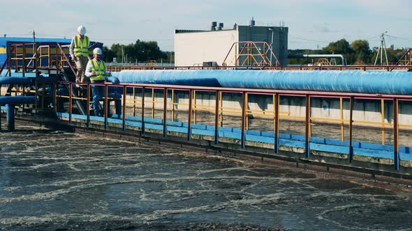 Two Wastewater Operators Walking Along Pipes at a Water Cleaning Plant