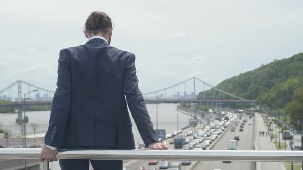 Back View of Desperate Depressed Caucasian Man Standing at Bridge Fence Ready To Jump Down on Urban