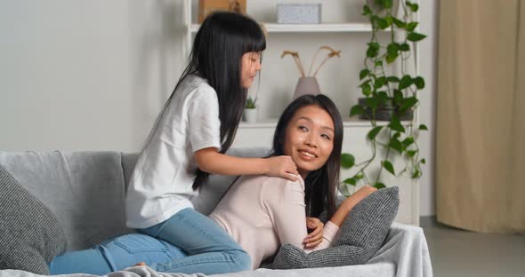 Asian Woman Young Loving Attentive Mother Lies on Couch Carries on Her Back Little Active Jumping