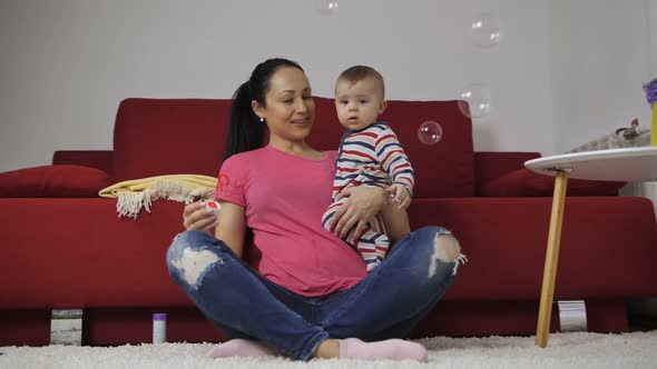 Mother Blowing Soap Bubbles with Baby at Home