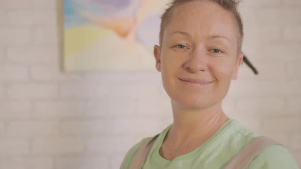 satisfied woman artist proudly hangs painted picture on wall