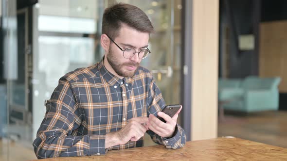 Serious Young Designer Using Smartphone in Office