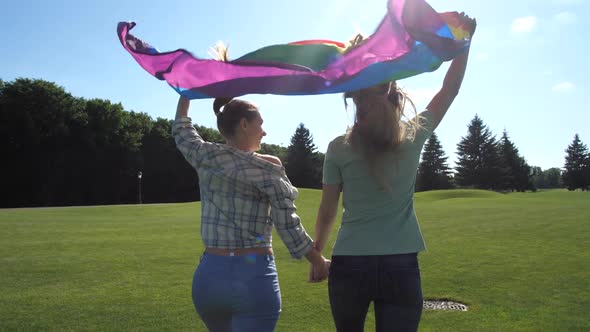 Young Lgbt Couple with Pride Flag Running in Park