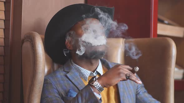 Black man smokes a cigar and the smoke released from the mouth