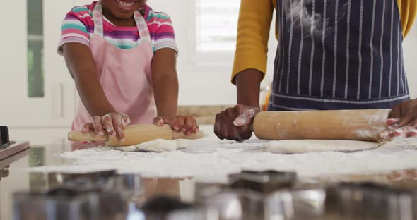 Happy african american mother and daughter rolling dough in kitchen