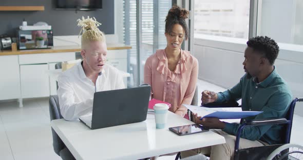 Diverse business people discussing with disabled colleague and documents in creative office