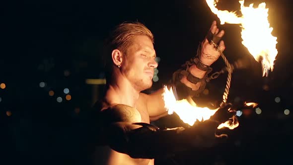 Young Blond Male Spins Two Burning Pois Around Face. Slow Motion Shot. Close-up Shot.