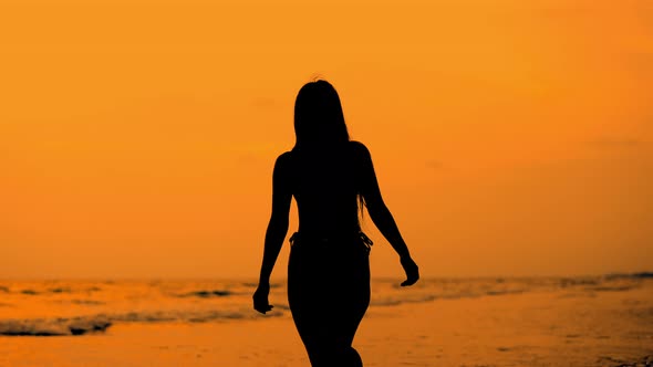 Silhouette Of Woman Running Along Golden Beach At Sunset