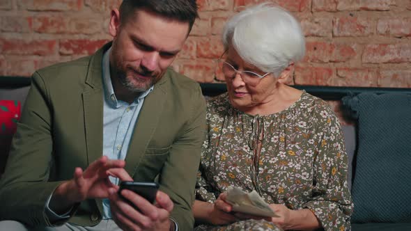 Two People From One Family Sitting on the Couch and Looking at Digital Photographs and Printed