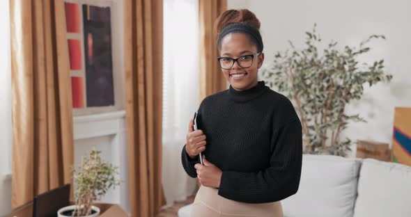 An Elegant Woman Holds a Tablet Under Her Arm in Hands Looks Into the Camera with a Smile Stands in