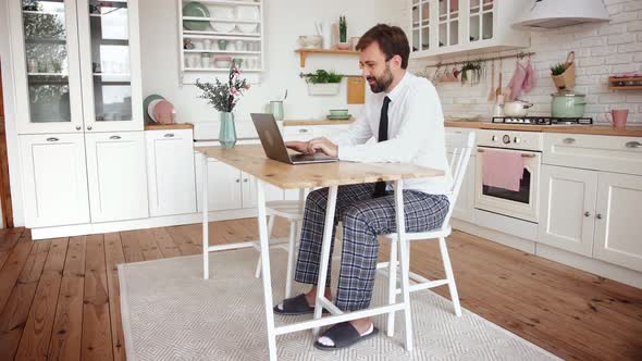 Young Bearded Man Working From Home with Laptop Wearing Shirt Tie and Pajama Pants in Kitchen Slow