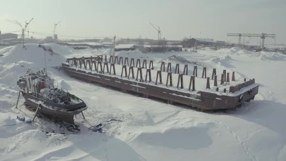 Aerial view of an old pier and a moored rusty ship on a snow covered shore