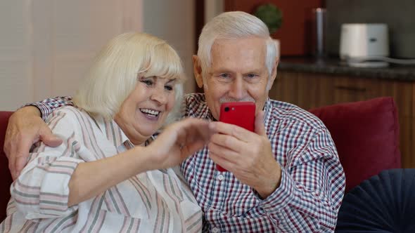 Grandmother and Grandfather Making Video Call Online on Mobile Phone at Home. Smiling Elderly Couple