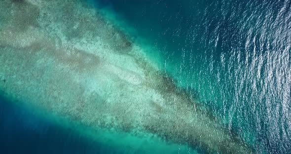 Daytime birds eye tourism shot of a white paradise beach and turquoise sea background in vibrant 4K