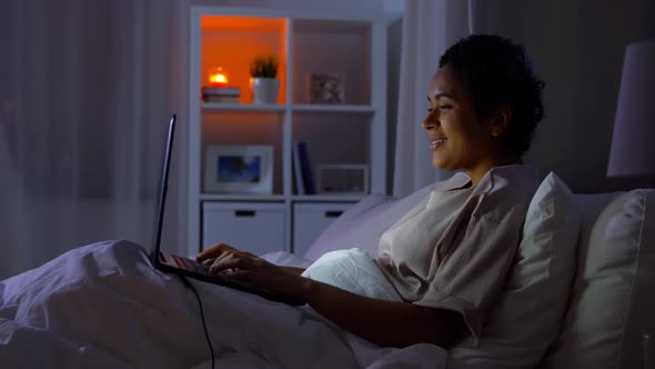 Woman with Laptop in Bed at Home at Night