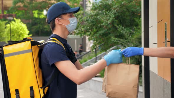 Delivery Man Wears Protective Medical Face Mask and Gloves Picks Up Paper Bag