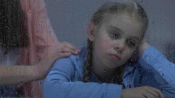 Mother Stroking Gently Upset Little Daughter Sitting Near Rainy Window, Support