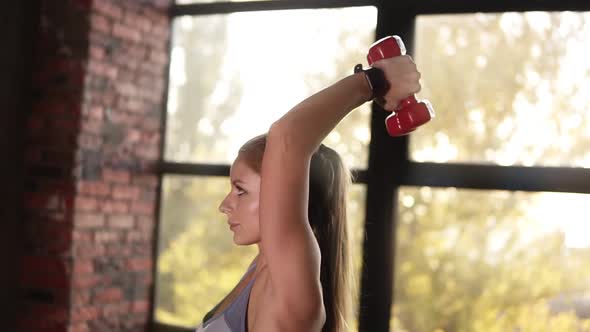 Young Sporty Woman is Doing Physical Exercise with Weights in Hands