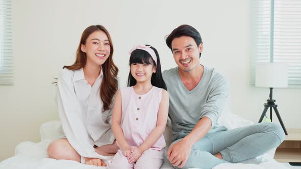 Portrait of Asian happy family smile and look at camera on bed together in bedroom at home.